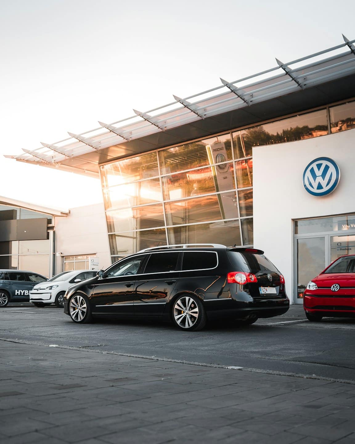Black Volkswagen station wagon parked at dealership at sunset.
